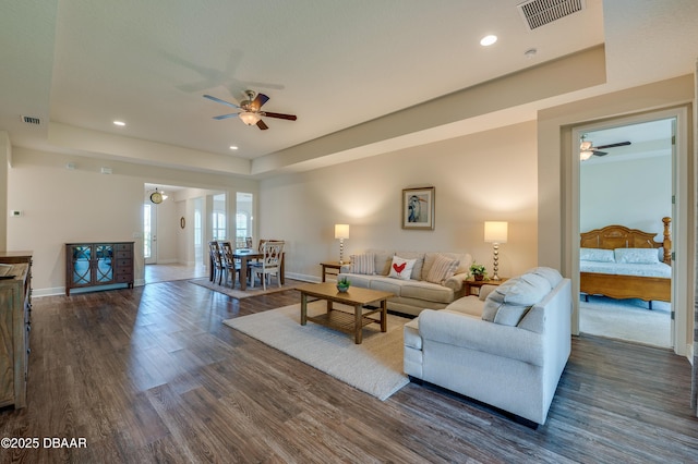 living room featuring a raised ceiling, dark wood-type flooring, and ceiling fan