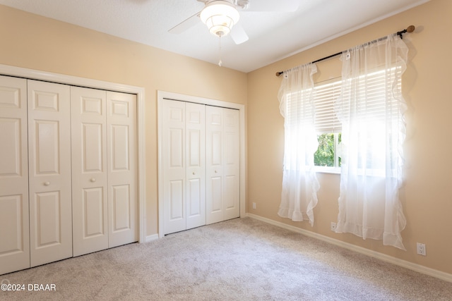 unfurnished bedroom with ceiling fan, light colored carpet, and multiple closets