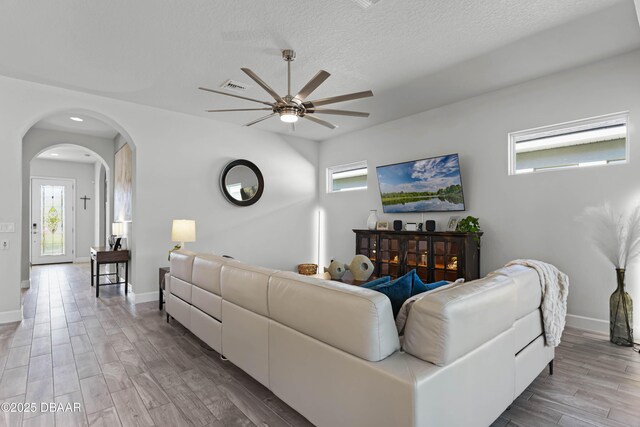 living room featuring wood-type flooring, ceiling fan with notable chandelier, and a textured ceiling