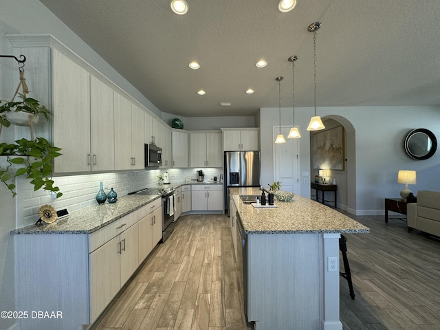 kitchen featuring light hardwood / wood-style flooring, stainless steel appliances, decorative light fixtures, a kitchen island with sink, and white cabinets