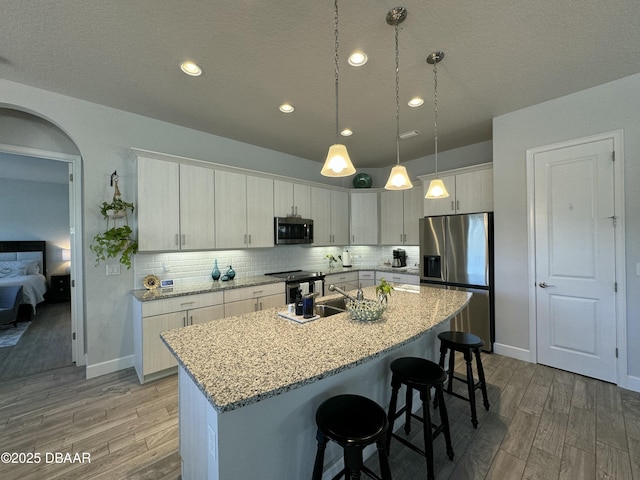 kitchen with decorative light fixtures, a kitchen island with sink, appliances with stainless steel finishes, and light stone counters