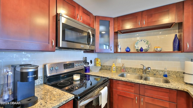 kitchen featuring reddish brown cabinets, light stone counters, decorative backsplash, appliances with stainless steel finishes, and a sink