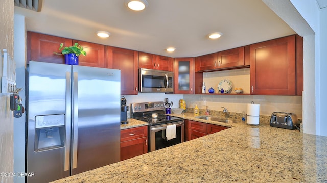 kitchen featuring light stone counters, stainless steel appliances, a sink, decorative backsplash, and glass insert cabinets