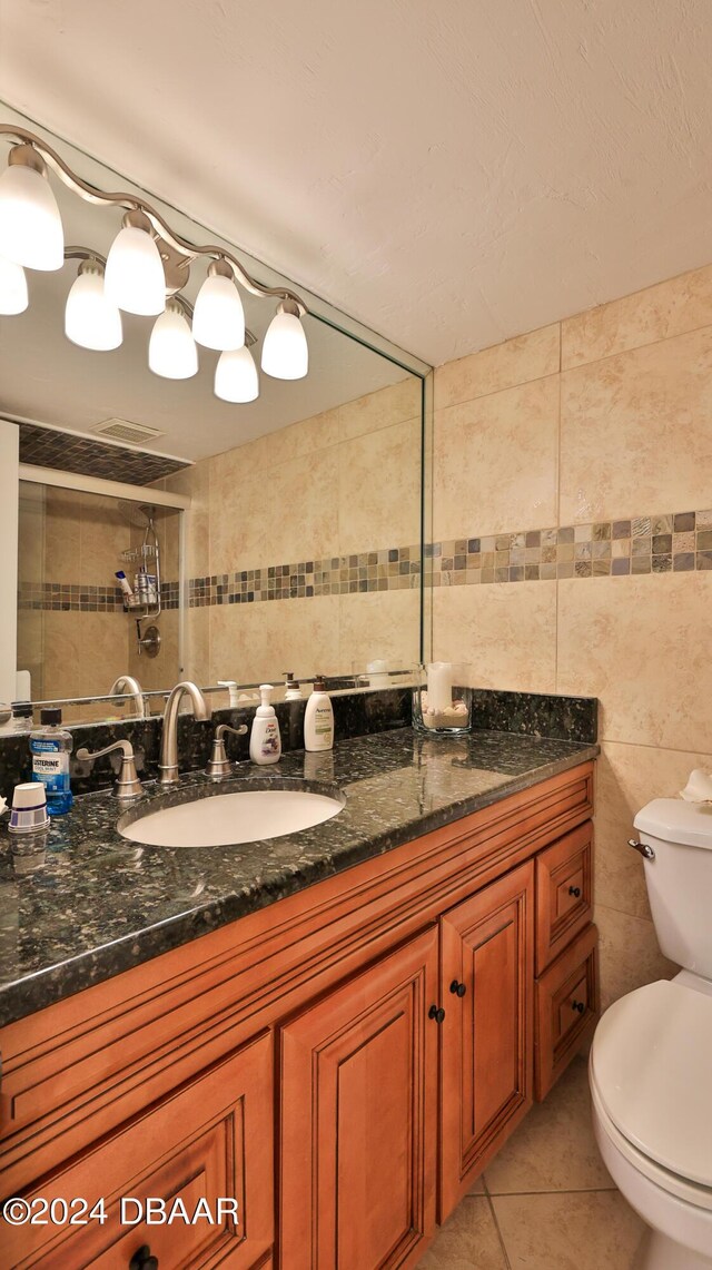 bathroom featuring tile walls, toilet, a tile shower, vanity, and tile patterned flooring