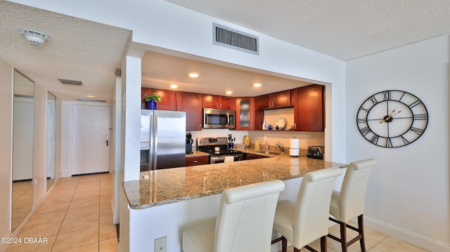 kitchen with light tile patterned flooring, stainless steel appliances, a peninsula, visible vents, and a kitchen breakfast bar