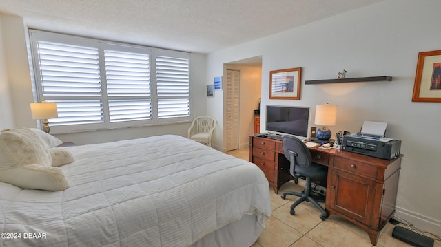 bedroom featuring a textured ceiling, a closet, light tile patterned flooring, and baseboards