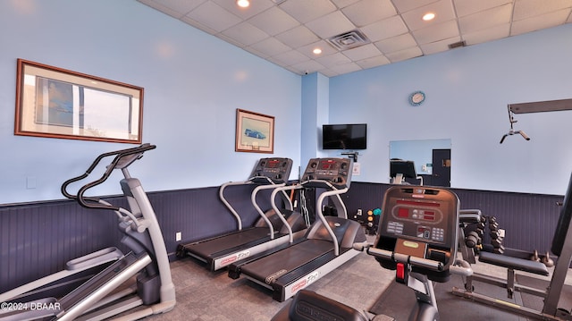 exercise room featuring a drop ceiling, wooden walls, carpet flooring, visible vents, and wainscoting