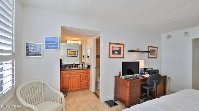 bedroom featuring light tile patterned floors, baseboards, ensuite bathroom, a textured ceiling, and a sink