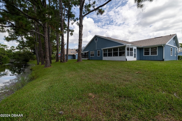 back of property with a sunroom, a water view, and a yard