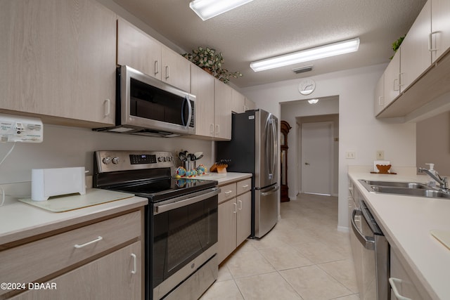 kitchen with appliances with stainless steel finishes, a textured ceiling, light tile patterned floors, light brown cabinets, and sink