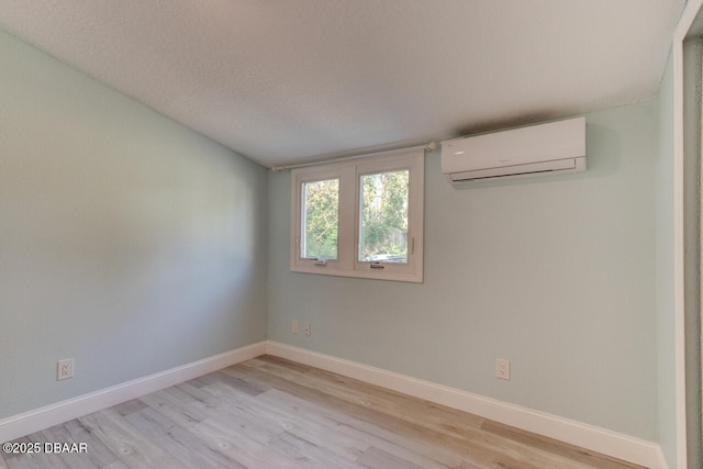 spare room with a wall mounted air conditioner, a textured ceiling, baseboards, and light wood-type flooring