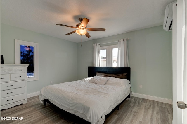 bedroom with baseboards, a ceiling fan, wood finished floors, and a wall mounted AC