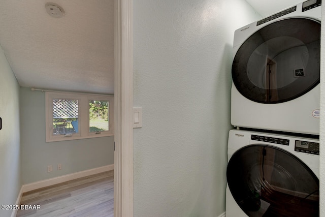 clothes washing area featuring baseboards, wood finished floors, stacked washer / dryer, and laundry area