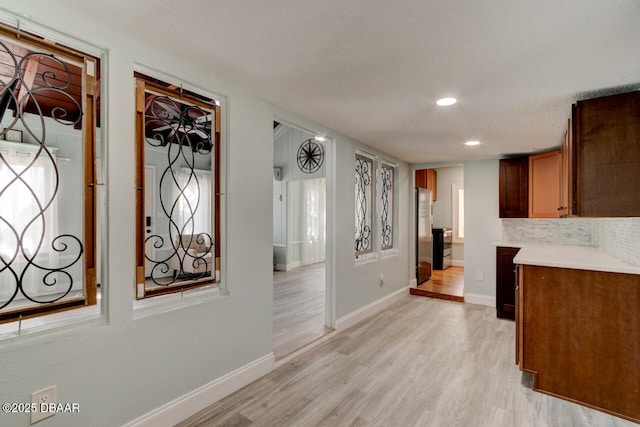 hallway with light wood-type flooring, baseboards, a textured ceiling, and recessed lighting