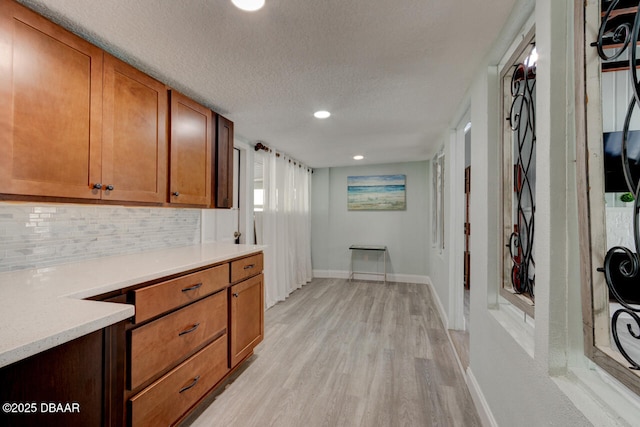 interior space featuring decorative backsplash, brown cabinets, light wood-type flooring, light countertops, and baseboards