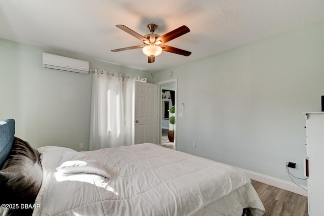 bedroom with baseboards, a ceiling fan, wood finished floors, and a wall unit AC