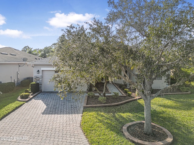 view of property hidden behind natural elements featuring a garage, stucco siding, decorative driveway, and a front yard