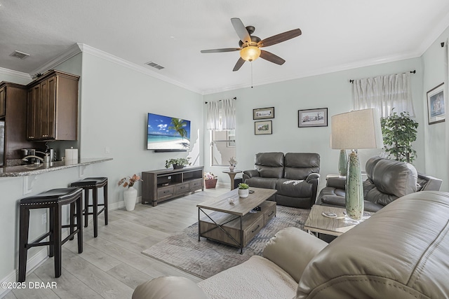 living room with baseboards, visible vents, light wood-style flooring, ceiling fan, and crown molding