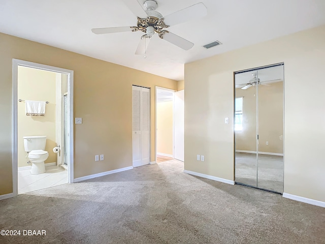 unfurnished bedroom featuring ensuite bath, ceiling fan, light colored carpet, and two closets