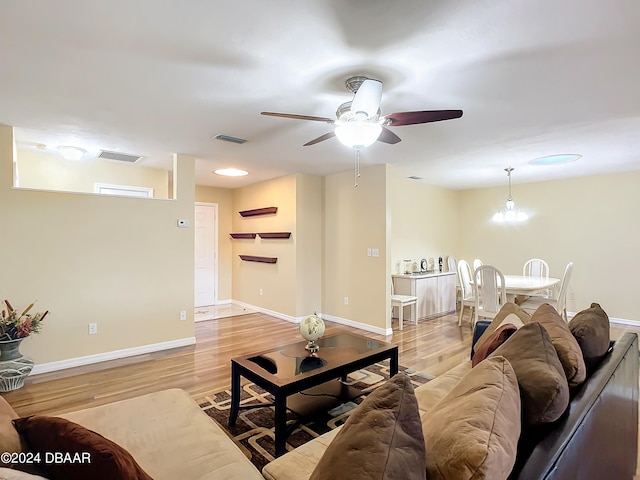 living room with ceiling fan with notable chandelier and light hardwood / wood-style floors