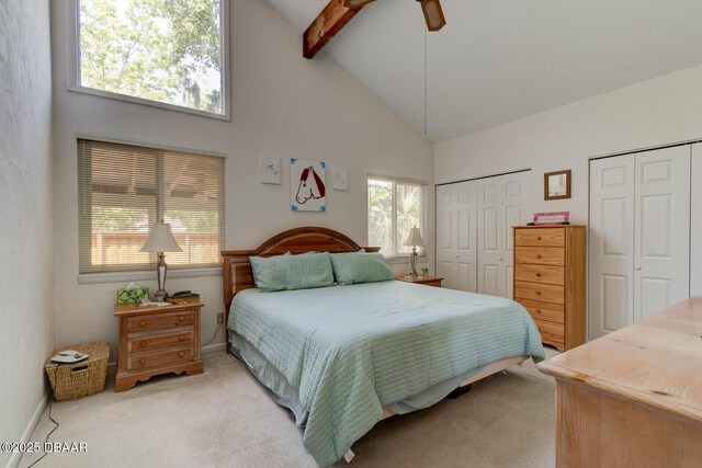 bedroom featuring two closets, high vaulted ceiling, light colored carpet, and beamed ceiling