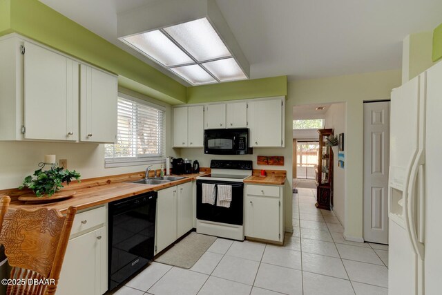 kitchen featuring white cabinets, a sink, butcher block countertops, light tile patterned floors, and black appliances