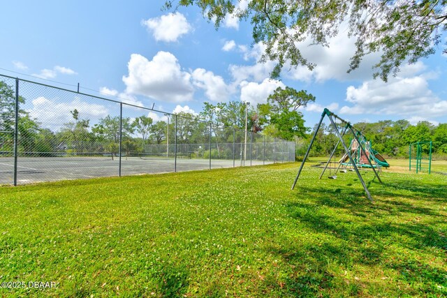 view of tennis court featuring a yard, playground community, and fence