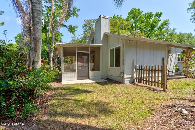 back of property with a sunroom, a yard, and a chimney