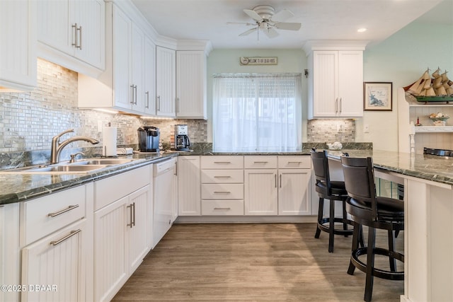 kitchen with sink, light hardwood / wood-style flooring, dishwasher, dark stone counters, and white cabinets