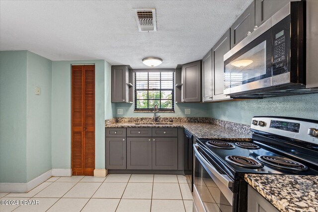 kitchen featuring gray cabinetry, stainless steel appliances, light tile patterned floors, sink, and dark stone countertops