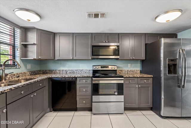 kitchen featuring gray cabinetry, appliances with stainless steel finishes, a textured ceiling, stone counters, and sink