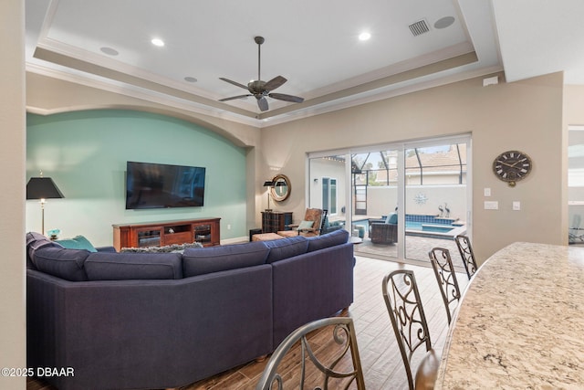 living room featuring a raised ceiling, wood-type flooring, crown molding, and ceiling fan