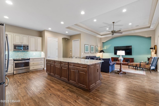 kitchen featuring a center island with sink, dark brown cabinets, a raised ceiling, dark wood-type flooring, and appliances with stainless steel finishes