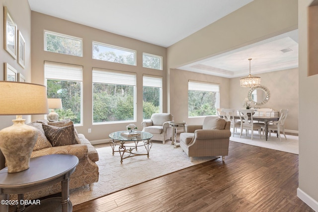 living room featuring dark hardwood / wood-style flooring, a raised ceiling, and a notable chandelier