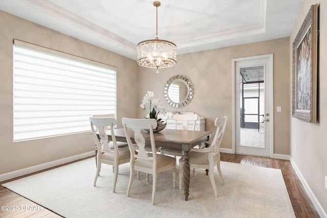 dining space featuring hardwood / wood-style flooring, a tray ceiling, and a notable chandelier