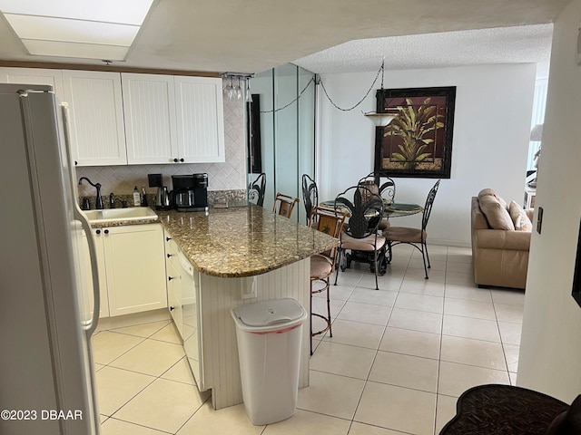 kitchen featuring tasteful backsplash, white fridge, dark stone counters, sink, and white cabinets