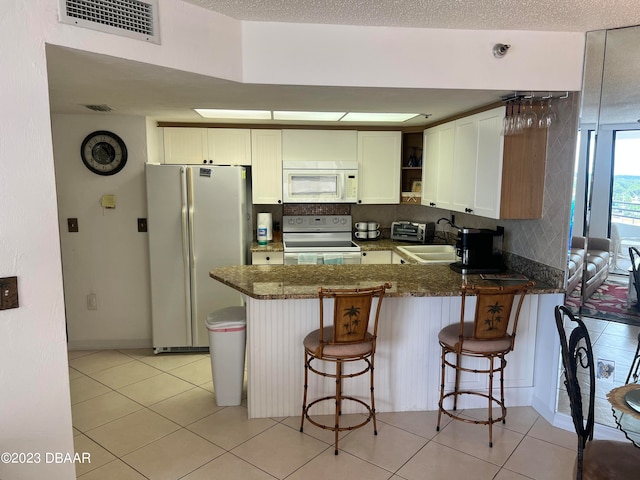 kitchen featuring white cabinets, white appliances, a kitchen bar, and kitchen peninsula