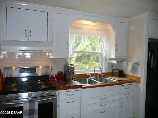 kitchen with freestanding refrigerator, under cabinet range hood, stainless steel range with gas cooktop, white cabinetry, and a sink