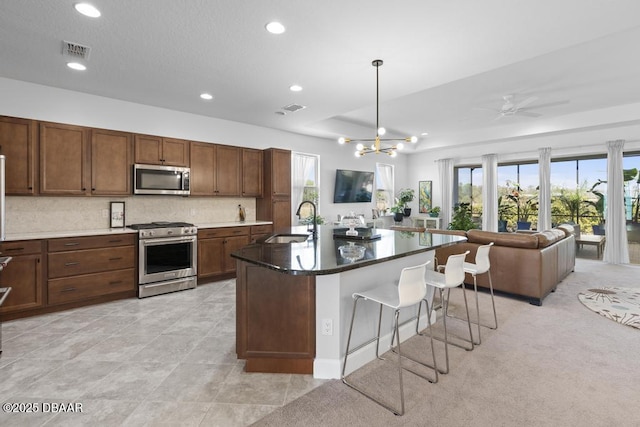 kitchen with sink, appliances with stainless steel finishes, a kitchen breakfast bar, a center island with sink, and decorative backsplash