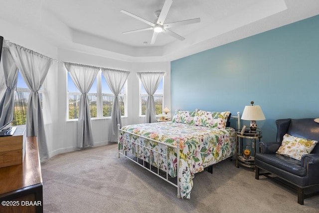 carpeted bedroom with a raised ceiling and ceiling fan