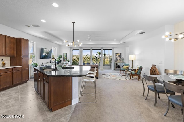 kitchen with sink, a tray ceiling, a chandelier, and a center island with sink