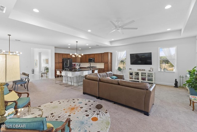 living room with a raised ceiling, ceiling fan with notable chandelier, and light carpet