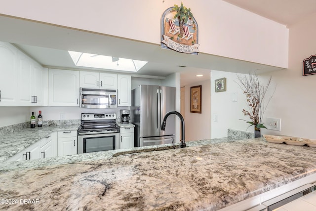 kitchen featuring white cabinets, kitchen peninsula, light stone countertops, and stainless steel appliances