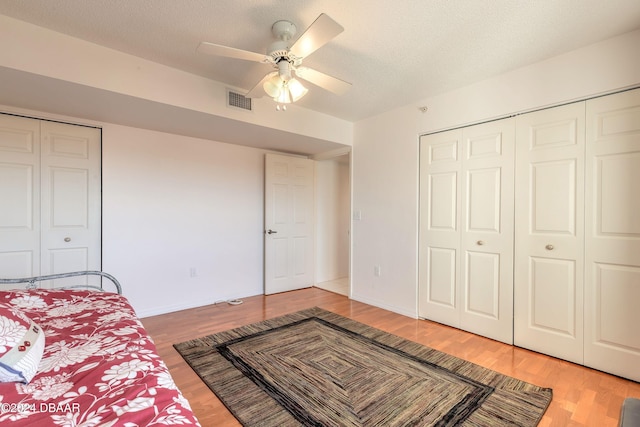 bedroom with a textured ceiling, ceiling fan, two closets, and hardwood / wood-style flooring