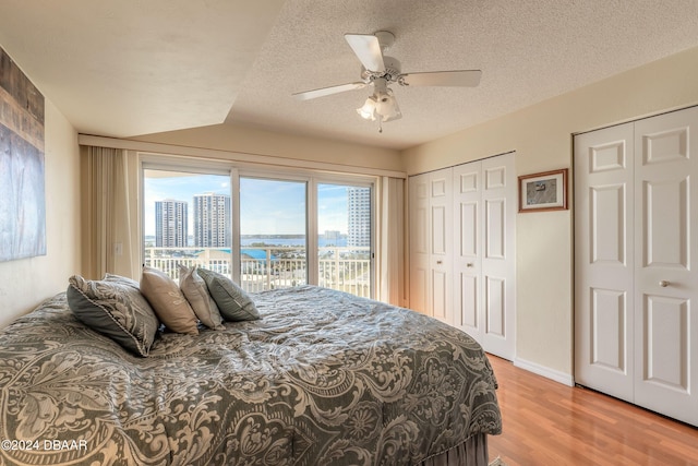 bedroom featuring two closets, hardwood / wood-style floors, ceiling fan, access to exterior, and a textured ceiling