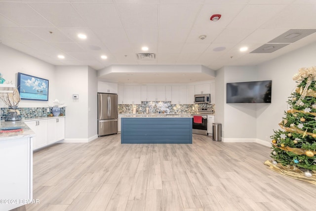 kitchen with a center island, white cabinetry, stainless steel appliances, decorative backsplash, and a drop ceiling