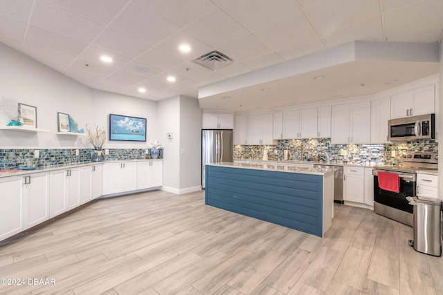 kitchen with white cabinets, appliances with stainless steel finishes, a center island, light wood-type flooring, and a drop ceiling