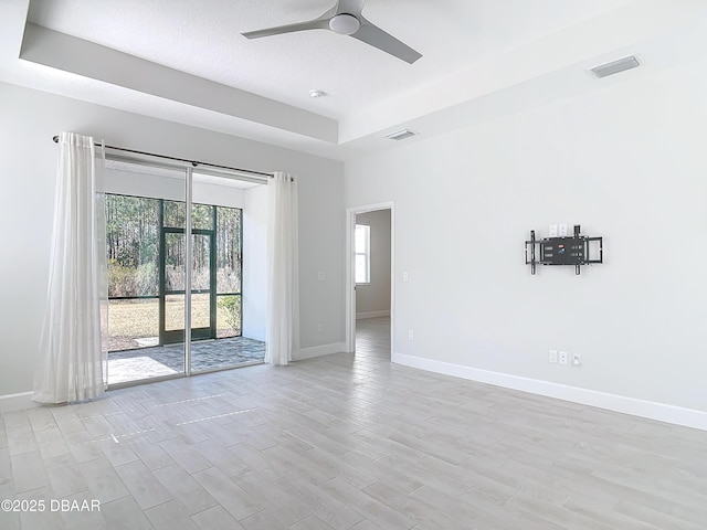 spare room with a raised ceiling, ceiling fan, and light hardwood / wood-style flooring