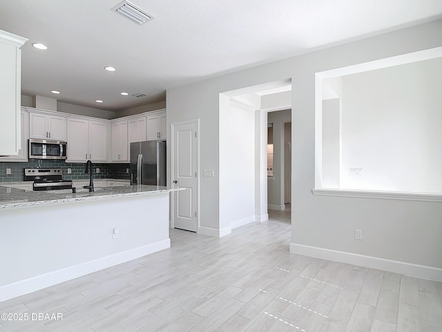 kitchen featuring tasteful backsplash, kitchen peninsula, stainless steel appliances, light stone countertops, and white cabinets