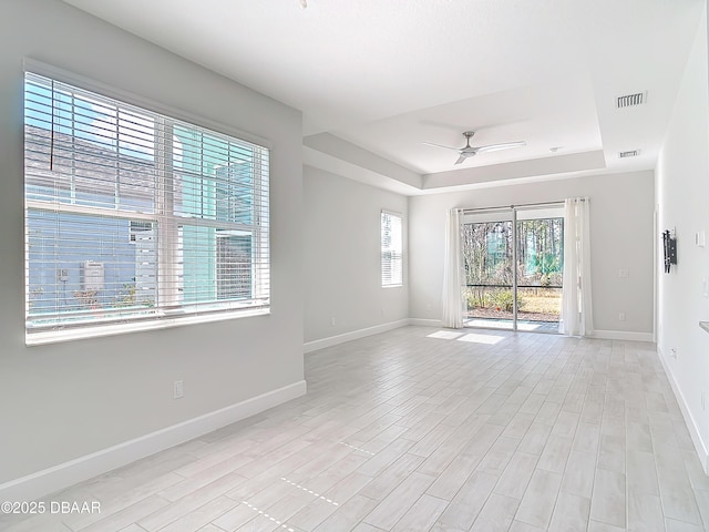 empty room with a raised ceiling, ceiling fan, and light hardwood / wood-style flooring